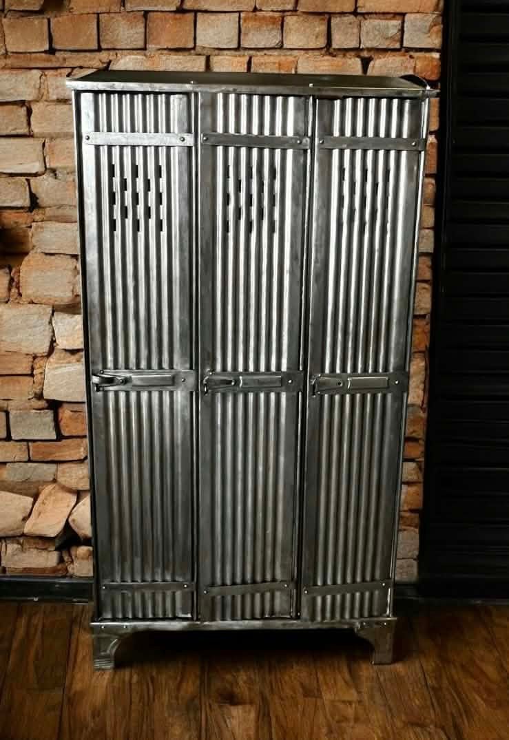 Vestiaire industriel 3 portes en tôle ondulée, métal brut poli, devant un mur en pierre
